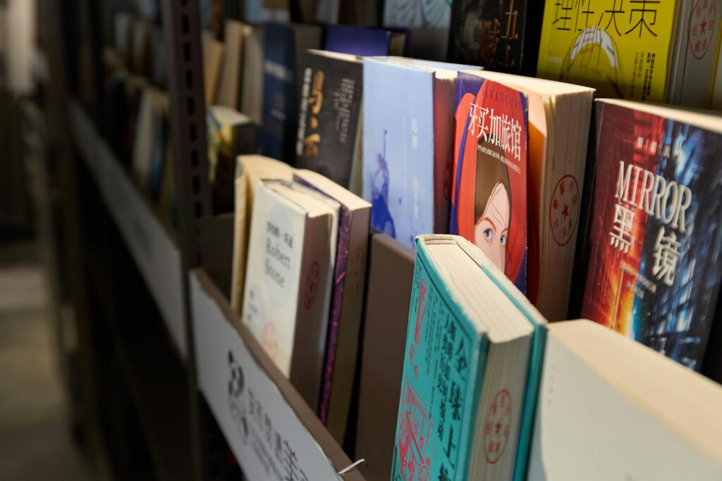 Books neatly arranged on a library shelf, showcasing a variety of genres and languages.